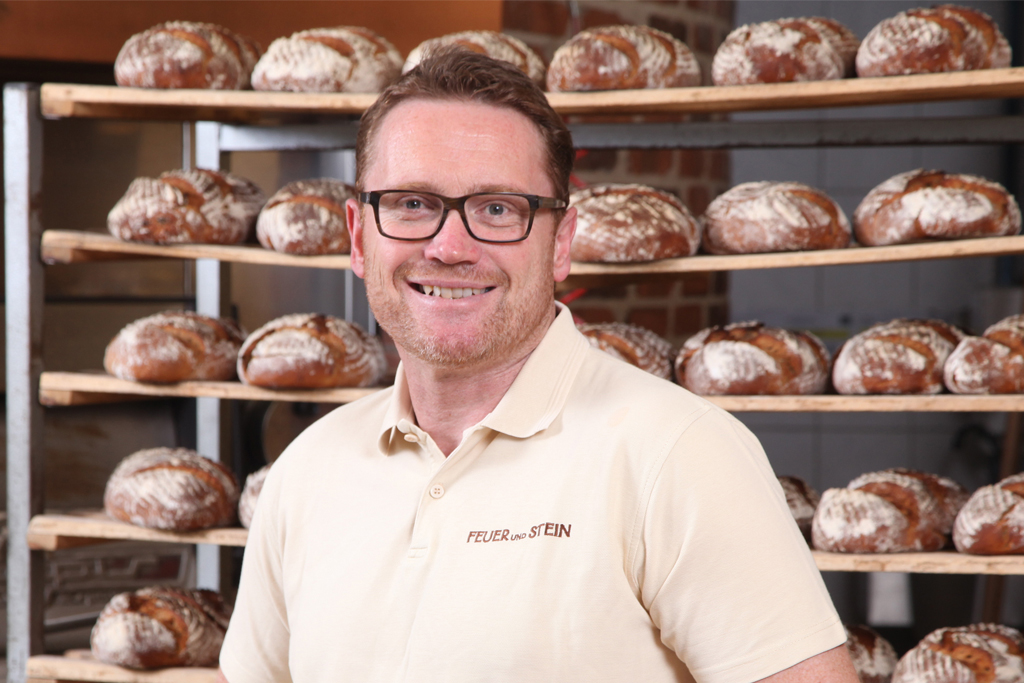 Porträt von Jürgen Iwan, Geschäftsführer der Bäckerei Grund vor einem Brotregal